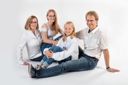 familienfoto auf weißem hintergrund die familie sitzt am boden ineinander verschachtelst sie tragen jeans mit weißen oberteilen