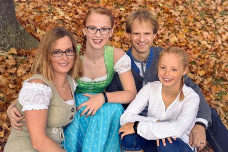 familienfoto mit mutter vater und zwei schwestern alle in tracht sie sitzen im herbstlichen laub eng zusammen und lachen