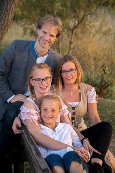 familenfoto bei sonnenuntergang die familie sitzt auf einer parkbank alle kuscheln miteinander im hintergrund eine weide