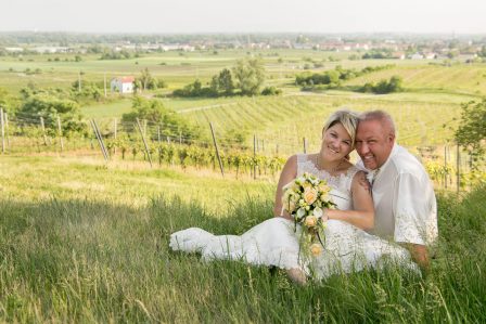 hochzeitsfoto brautpaar sitzt auf der weinbergkuppe im hintergrund der nächstgelegene ort